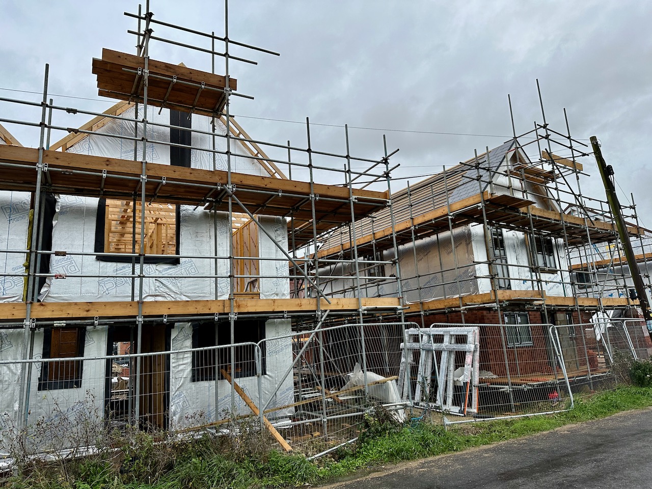 A pair of timber-framed new build houses under construction, wrapped in a reflective weatherproof membrane for insulation and energy efficiency.